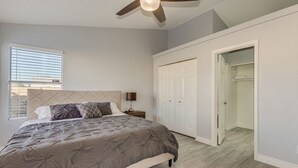 A bedroom with a bed, a ceiling fan, a window with blinds, a wardrobe, and a door leading to another room. - Beautiful remodeled home to enjoy your stay. (Phoenix)