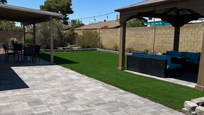 A patio area with stone flooring, a grassy lawn, and outdoor furniture under pergolas. - Beautiful remodeled home to enjoy your stay. (Phoenix)
