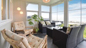 A sunlit room with wicker furniture, large windows, and a view of the sea.