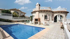 A pool area with a tiled deck, outdoor seating, and a stone building with a chimney.