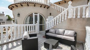 A balcony with wicker furniture, a white balustrade, and a tiled floor.