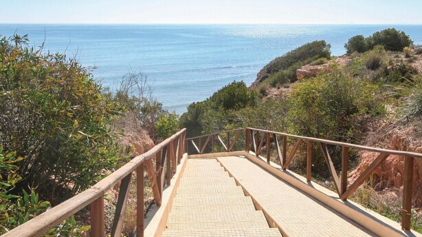 A wooden staircase leading to a viewpoint overlooking a coastal area with a clear view of the sea.