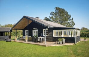 Une maison en bois noire dotée d’un patio couvert, d’un coin repas et d’une grande fenêtre donnant sur la cour.