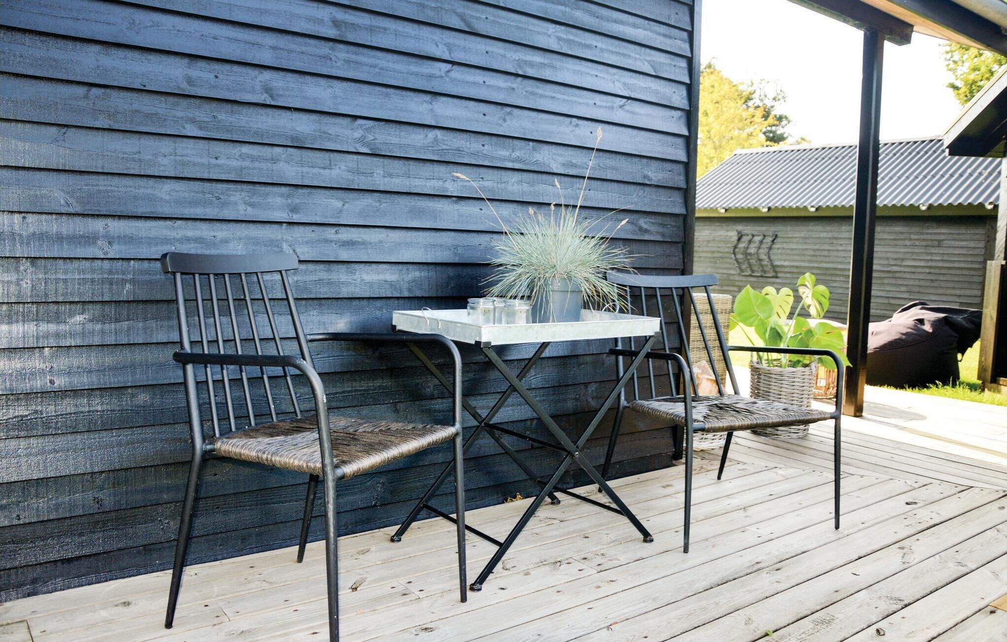A wooden deck with two metal chairs and a small table, a potted plant, and a bag on the ground.