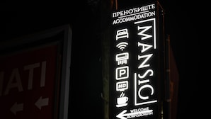 A neon sign for "MANSIC" accommodation with icons indicating Wi-Fi, HD TV, and a coffee symbol. - Mansio (Niš)