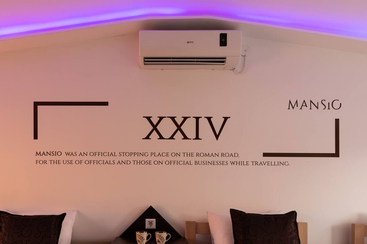 Una pared con el texto "MANSIO XXIV" y una descripción de Mansio como lugar de parada oficial en la Vía Romana.