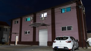 A white Renault Clio parked in front of a building with a garage door, air conditioning units, and a metal awning. - Mansio (Niš)