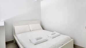 Une chambre d’hôtel minimaliste, avec un lit simple, du linge de lit blanc et une tête de lit sobre.