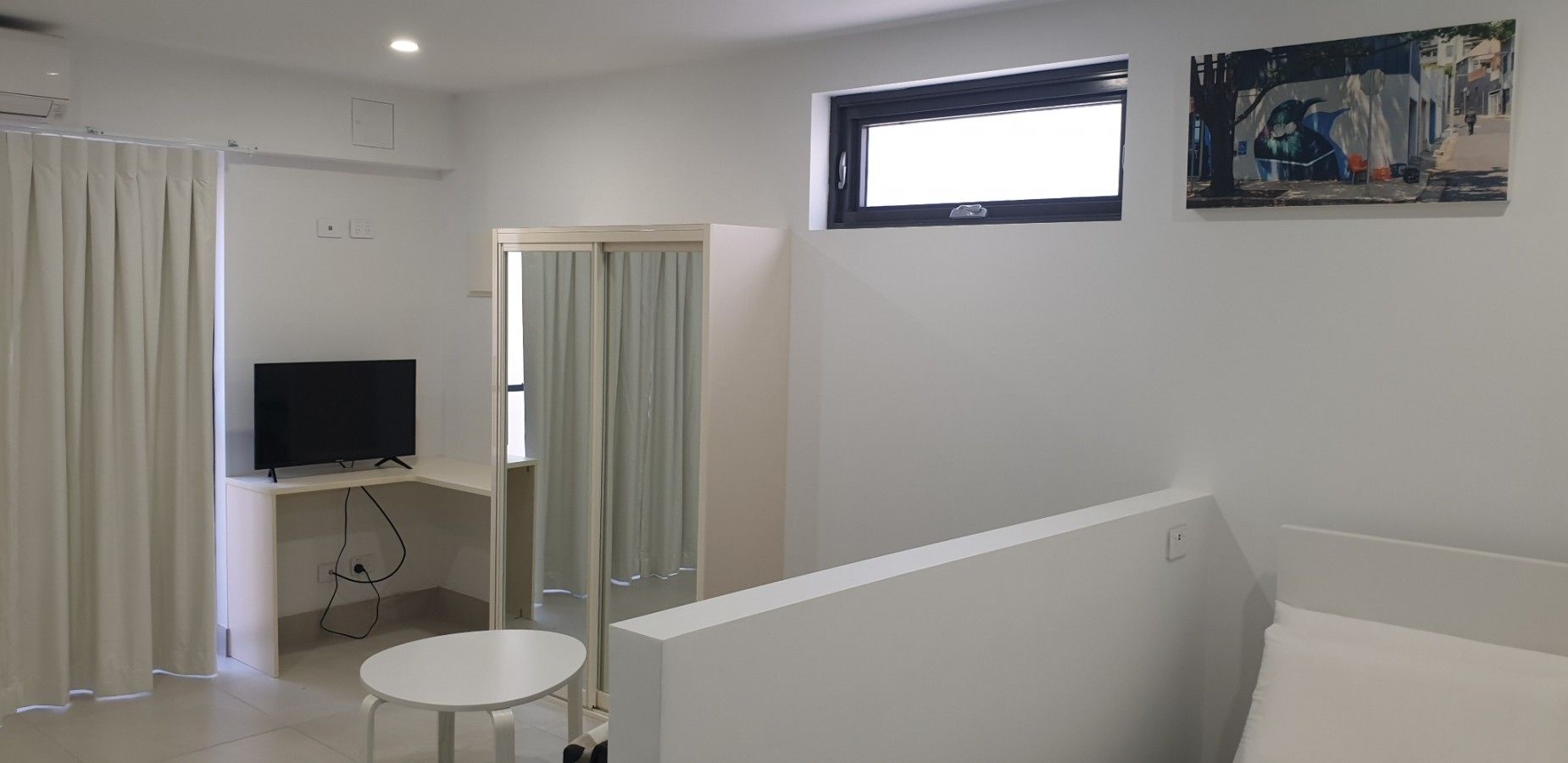 Een hotelkamer met een televisie, een tafeltje, een raam en een schilderij aan de muur.