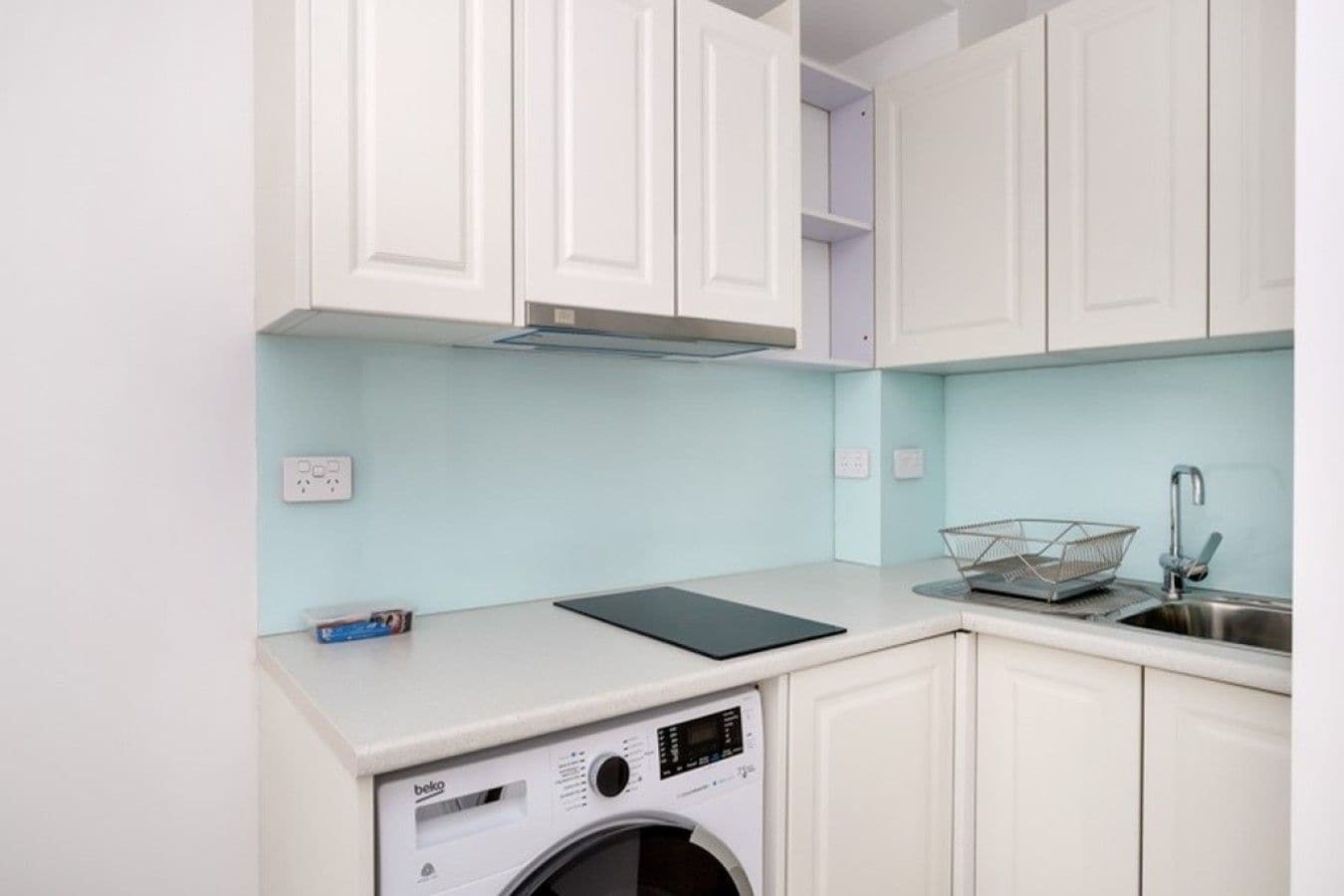 A compact kitchen with white cabinets, a washing machine, and a sink.