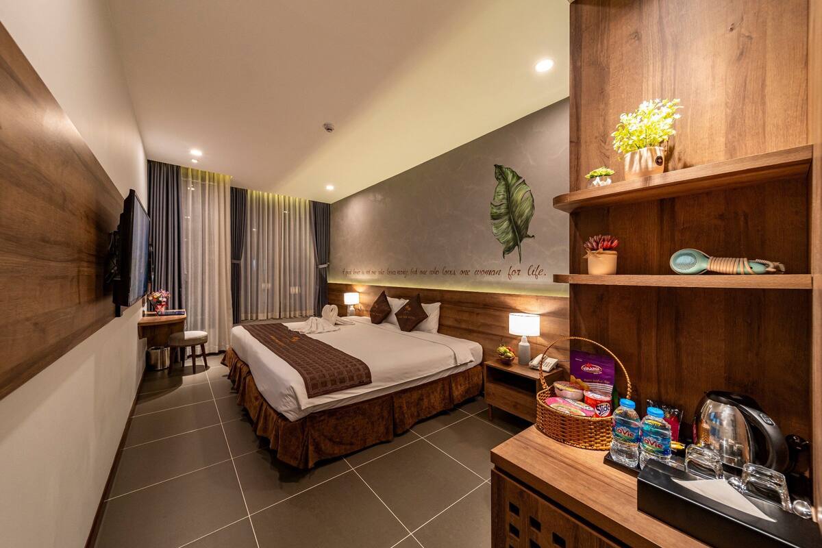 Ein Hotelzimmer mit einem großen Bett, einem Schreibtisch, einem Nachttisch und einem Holzboden mit Pflanzen.