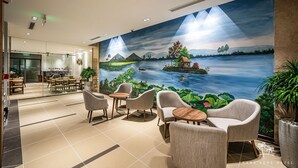 A hotel lobby with a mural of a serene landscape, comfortable seating, and a view of the restaurant area. - Thanh Long Hotel Bach Dang (Ho Chi Minh City)