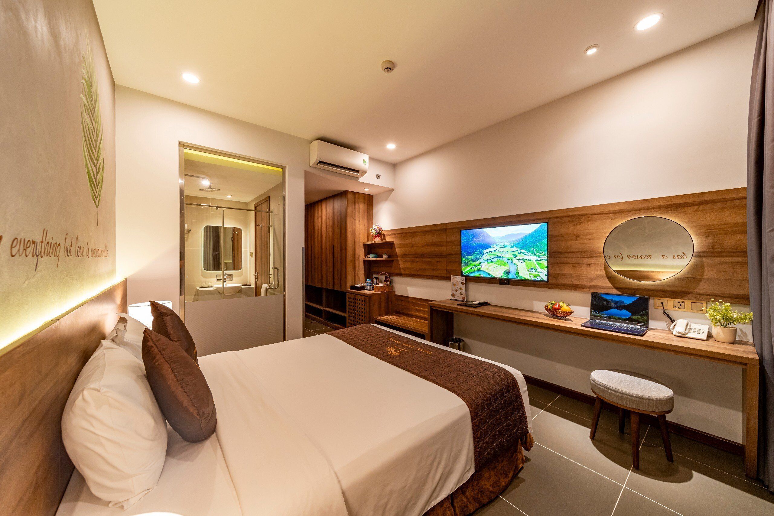 A modern hotel room with a large bed, a desk with a laptop, a television, and a mirror.