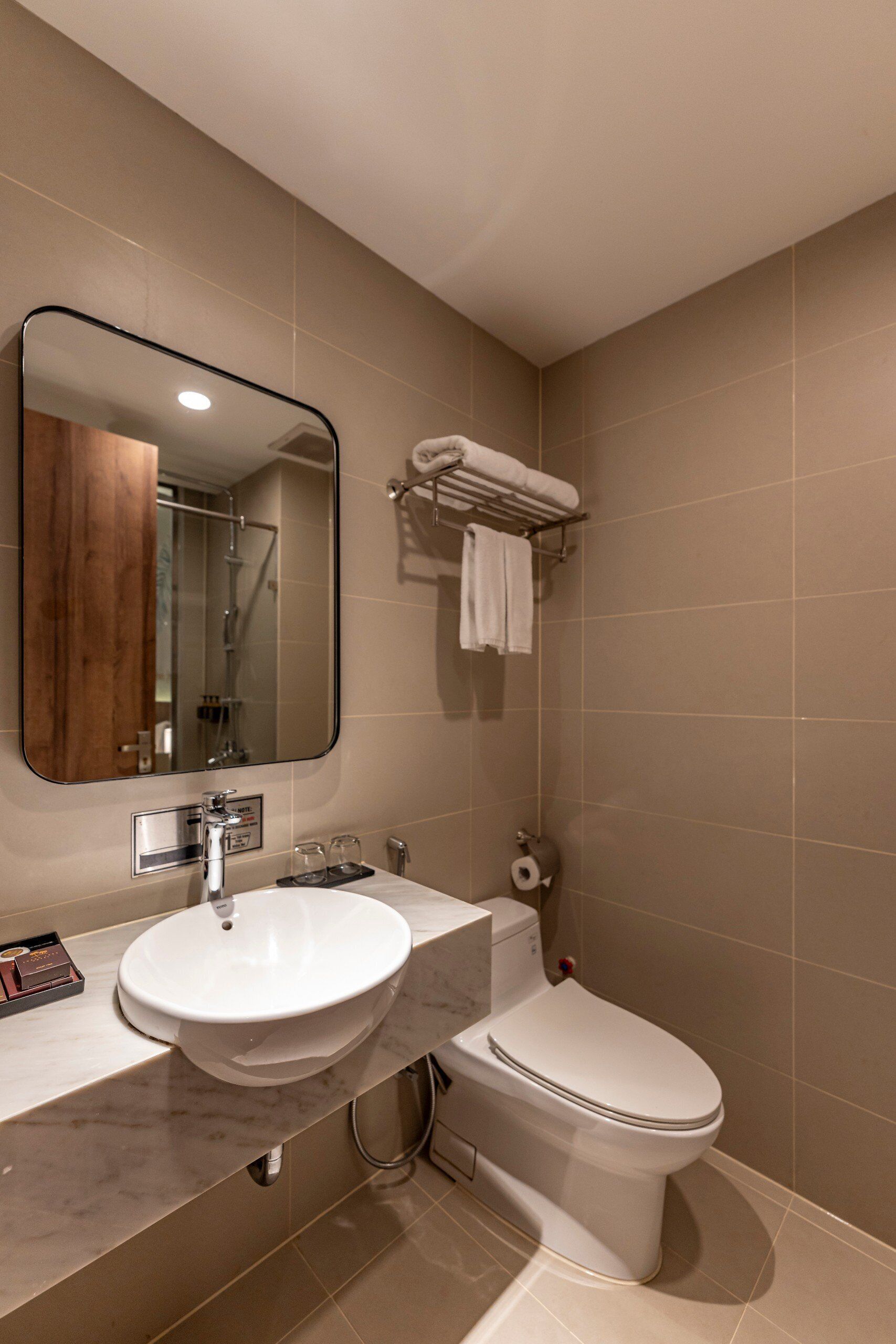 A modern bathroom with a sink, mirror, toilet, and towel rack.