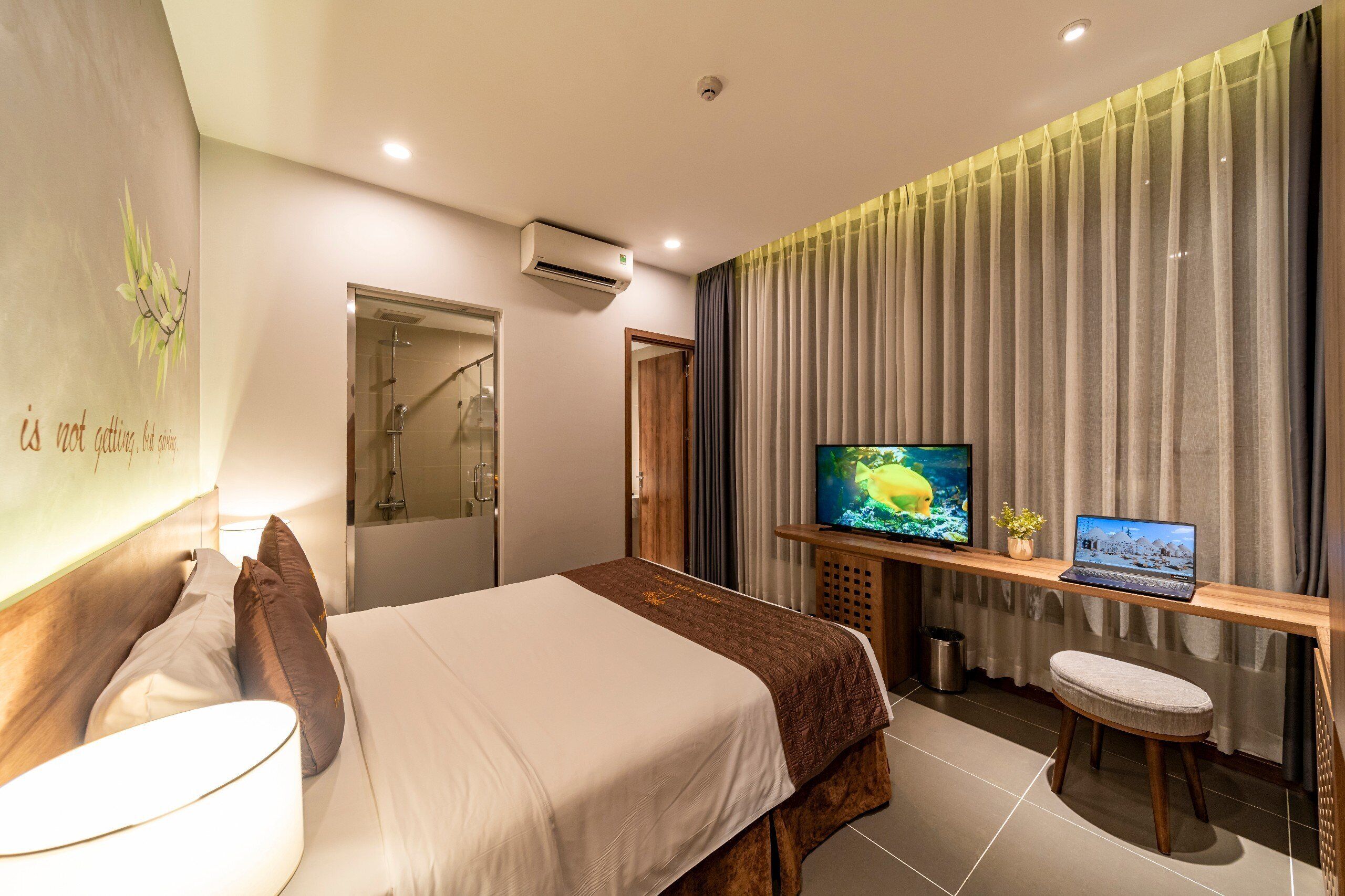 Hotellihuone, jossa on sänky, televisio, kannettava tietokone ja pieni jakkara.