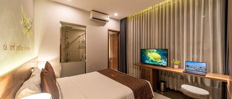 Una habitación de hotel con una cama, televisor, computadora portátil y un taburete pequeño.