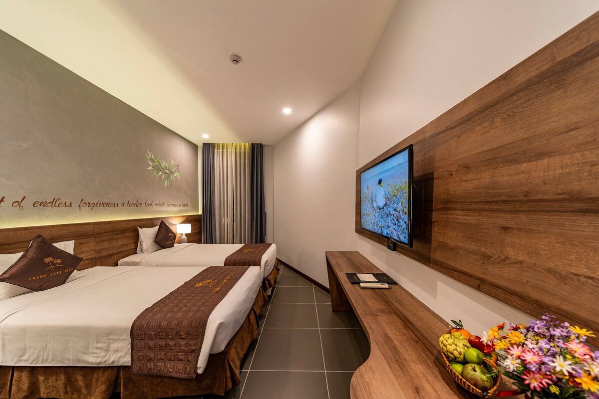 Ein Hotelzimmer mit zwei Betten, einem Fernseher, einer hölzernen Bank und einer Obstschale.