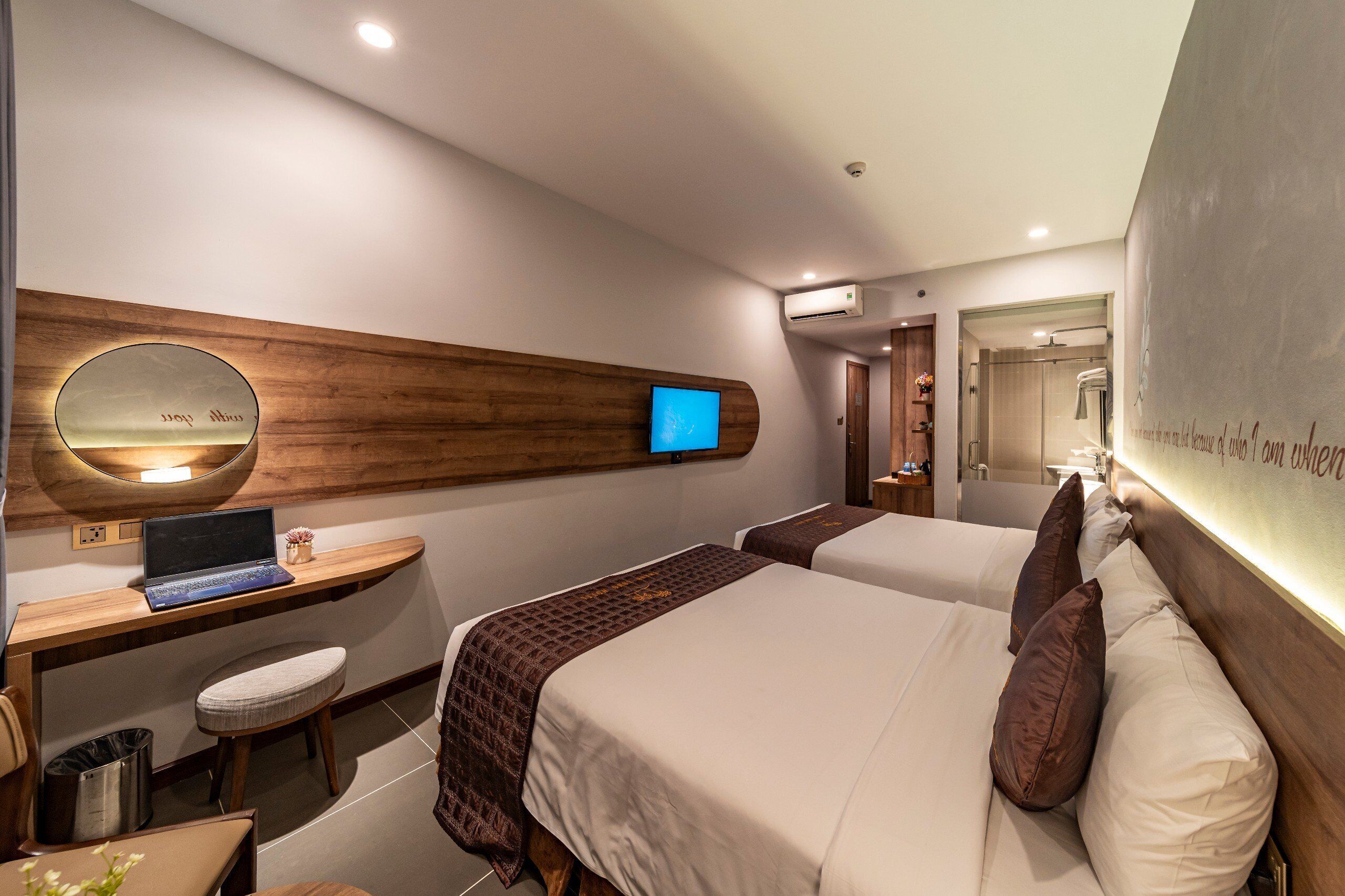 A hotel room with two beds, a desk with a laptop, a mirror, and an air conditioning unit.