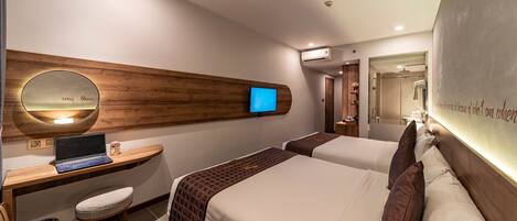A hotel room with two beds, a desk with a laptop, a mirror, and an air conditioning unit.