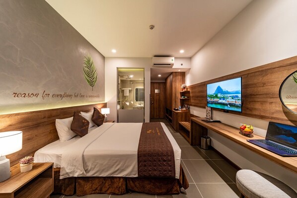 Una habitación de hotel moderna con una cama grande, un escritorio con una computadora portátil, un televisor y un aire acondicionado de pared.