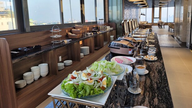 A buffet setup with a variety of dishes, including salads and hot foods, in a modern dining area with large windows and a high ceiling. - Thanh Long Hotel Bach Dang (Ho Chi Minh City)