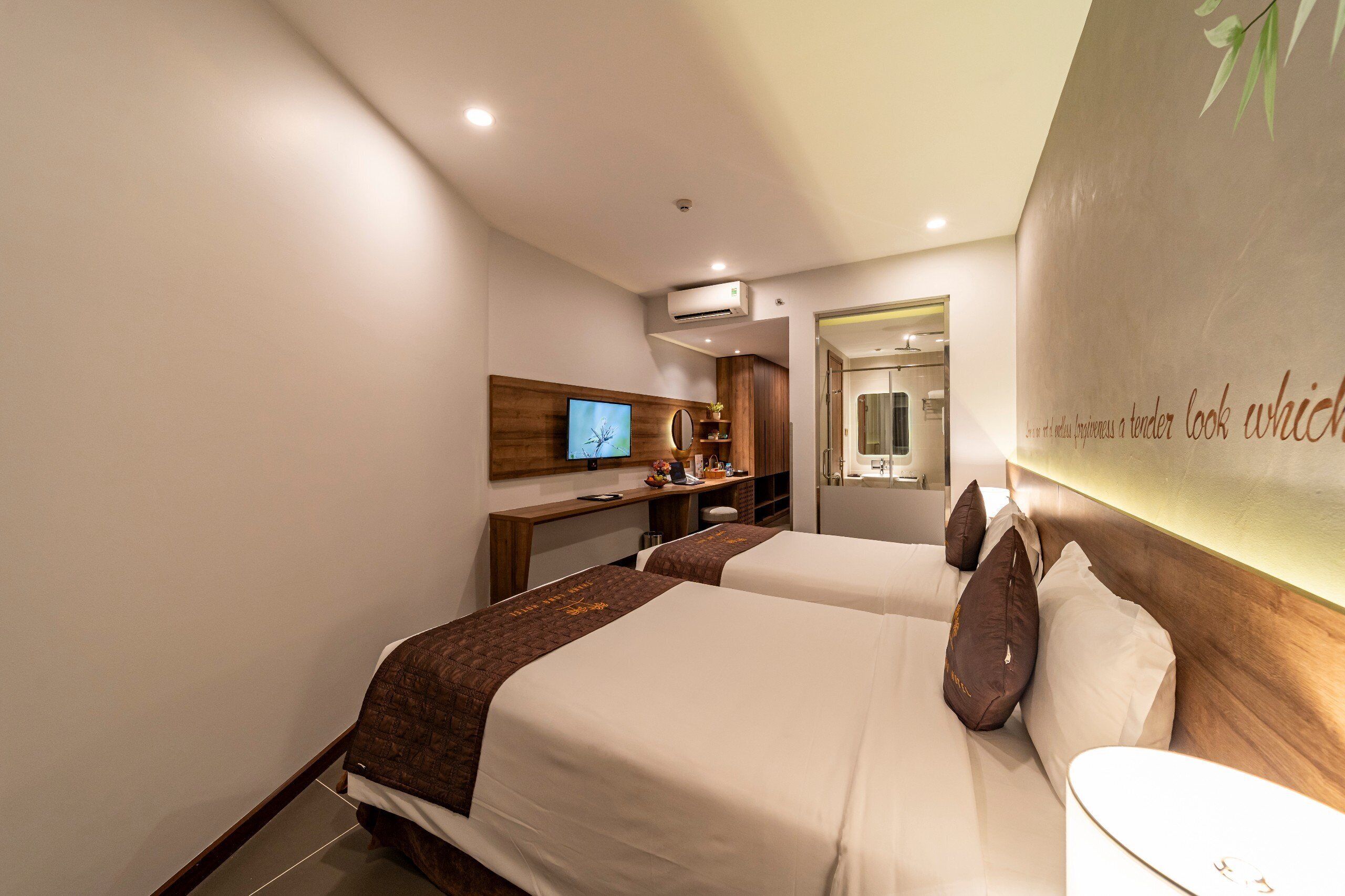 A hotel room with two beds, a desk, a television, and a bathroom.