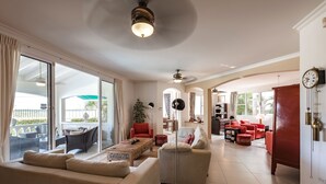 Amplia sala de estar con un sofá grande, una mesa de centro y un sillón rojo. Se observa un comedor con mesa y sillas, y una cocina al fondo.