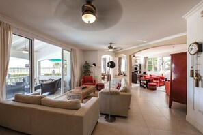 A spacious living room with a large sofa, a coffee table, and a red armchair. There is a dining area with a table and chairs, and a kitchen in the background. - Aruban villa in Nord, great view, cozy, safe, short drive to many beaches (Noord)