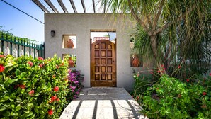 Una puerta de madera tradicional con un vestíbulo empedrado, rodeada de exuberante follaje y plantas florecientes.