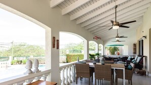 Un patio amplio con zona de comedor, columnas blancas y ventilador de techo.