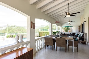 A spacious patio with a dining area, white columns, and a ceiling fan. - Aruban villa in Nord, great view, cozy, safe, short drive to many beaches (Noord)