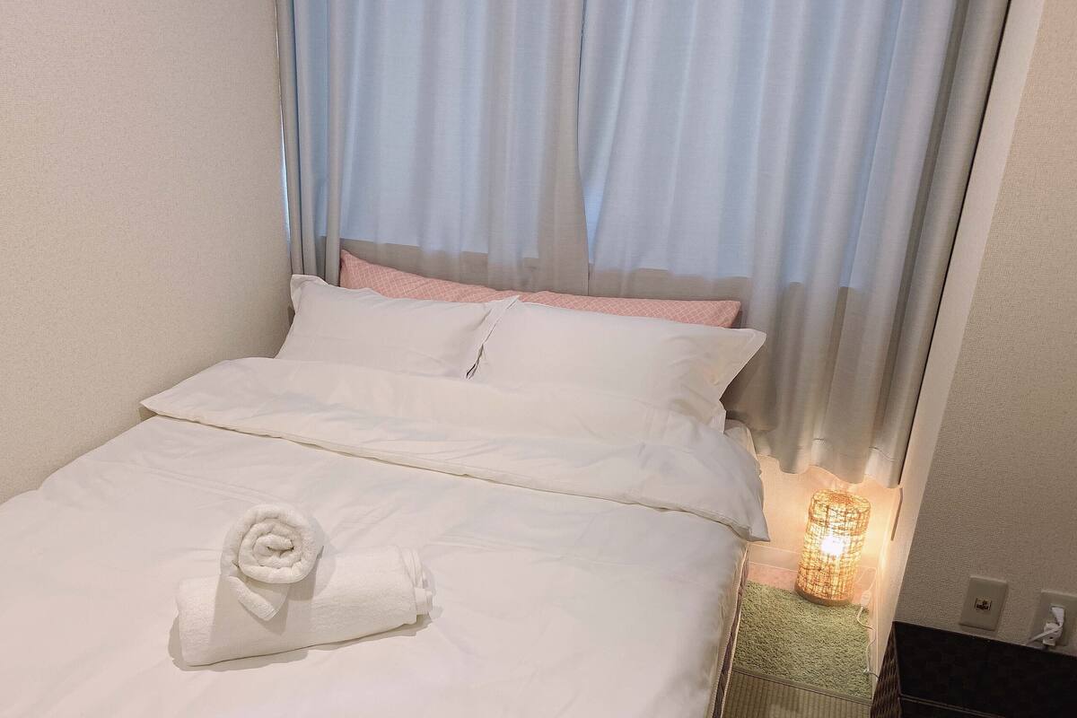 A neatly made bed with white linens, a rolled towel, and a small table lamp.