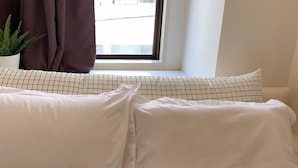 A white sofa with patterned cushions, a window with a view of buildings, and a potted plant on the left. - Hotel Minami (Tokyo)
