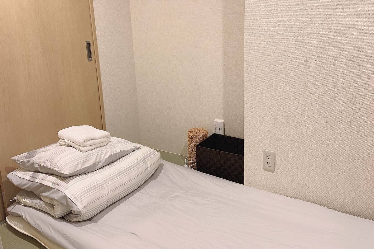 A bedroom with a bed, a wooden door, a wall-mounted air conditioner, and a small wicker basket.