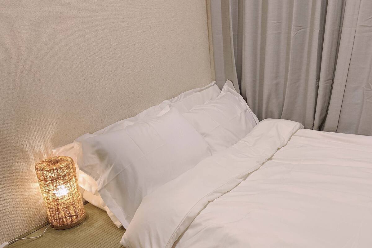 A neatly made bed with white linens and a single decorative light fixture beside it.