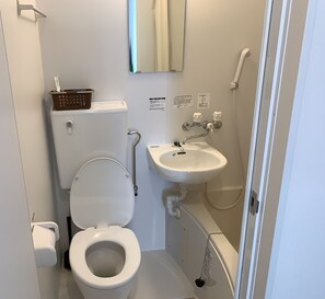 A small, compact bathroom with a toilet, sink, and a mirror. - Hotel Minami (Tokyo)