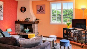 A cozy living room with a fireplace, a sofa, a TV, and a window with a view of greenery. - Awesome home in Surville with WiFi (Surville)