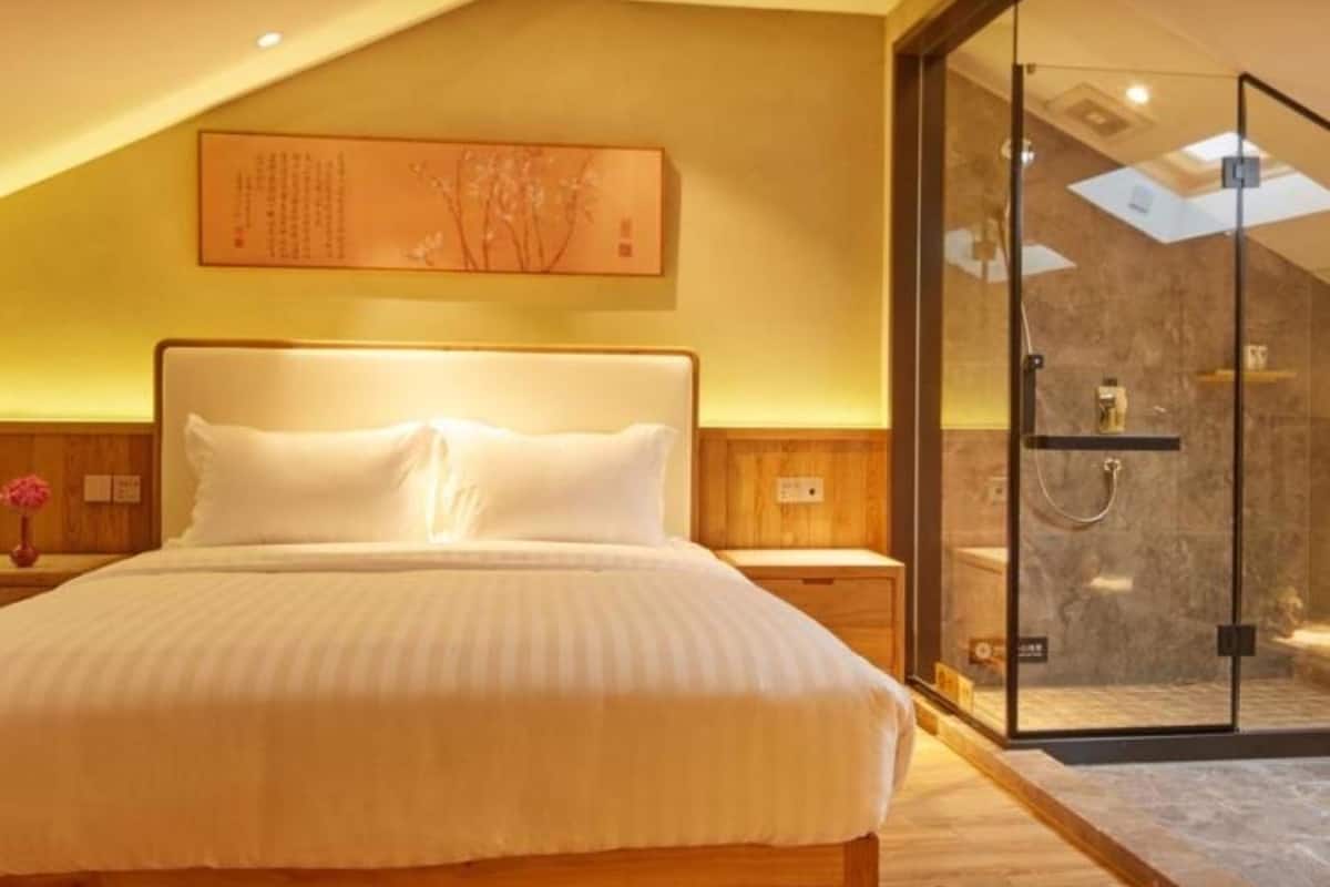 A modern bedroom with a large bed, wooden flooring, a glass shower enclosure, and a wall-mounted artwork.