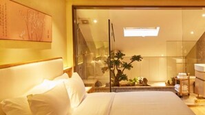 A large bed with white linens, a wooden headboard, and a glass door leading to a bathroom with a bathtub and a small plant. - Floral Hotel Joyful Garden Hangzhou (Hangzhou)