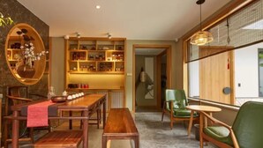 A dining area with a wooden table and benches, a green chair, and a shelf with various items. - Floral Hotel Joyful Garden Hangzhou (Hangzhou)