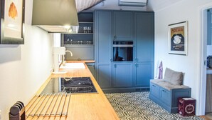 Een compacte keuken met een houten aanrechtblad, een inbouwfornuis en blauwe kastjes.