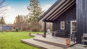 Een houten terras met buitenmeubilair, een overdekte veranda en uitzicht op een bebost gebied.