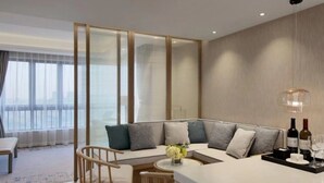 A modern living room with a sectional sofa, a small round table, and a bar area with glasses and bottles. - Oriental Ginza International Hotel (Dongguan)