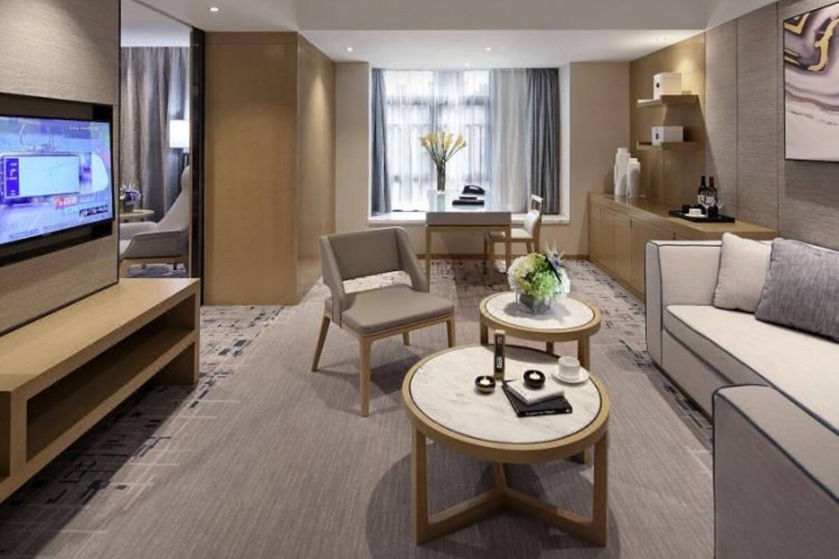Ein modernes Hotelzimmer mit Flachbildfernseher, einer Couch, einem Esstisch mit Stühlen und einem kleinen runden Tisch mit Blumen.