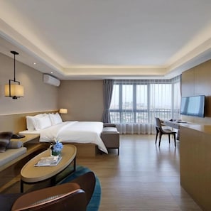 A hotel room with a bed, a desk, a chair, a sofa, and a TV.