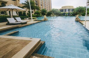 A swimming pool with lounge chairs and a statue, surrounded by palm trees and buildings. - Oriental Ginza International Hotel (Dongguan)