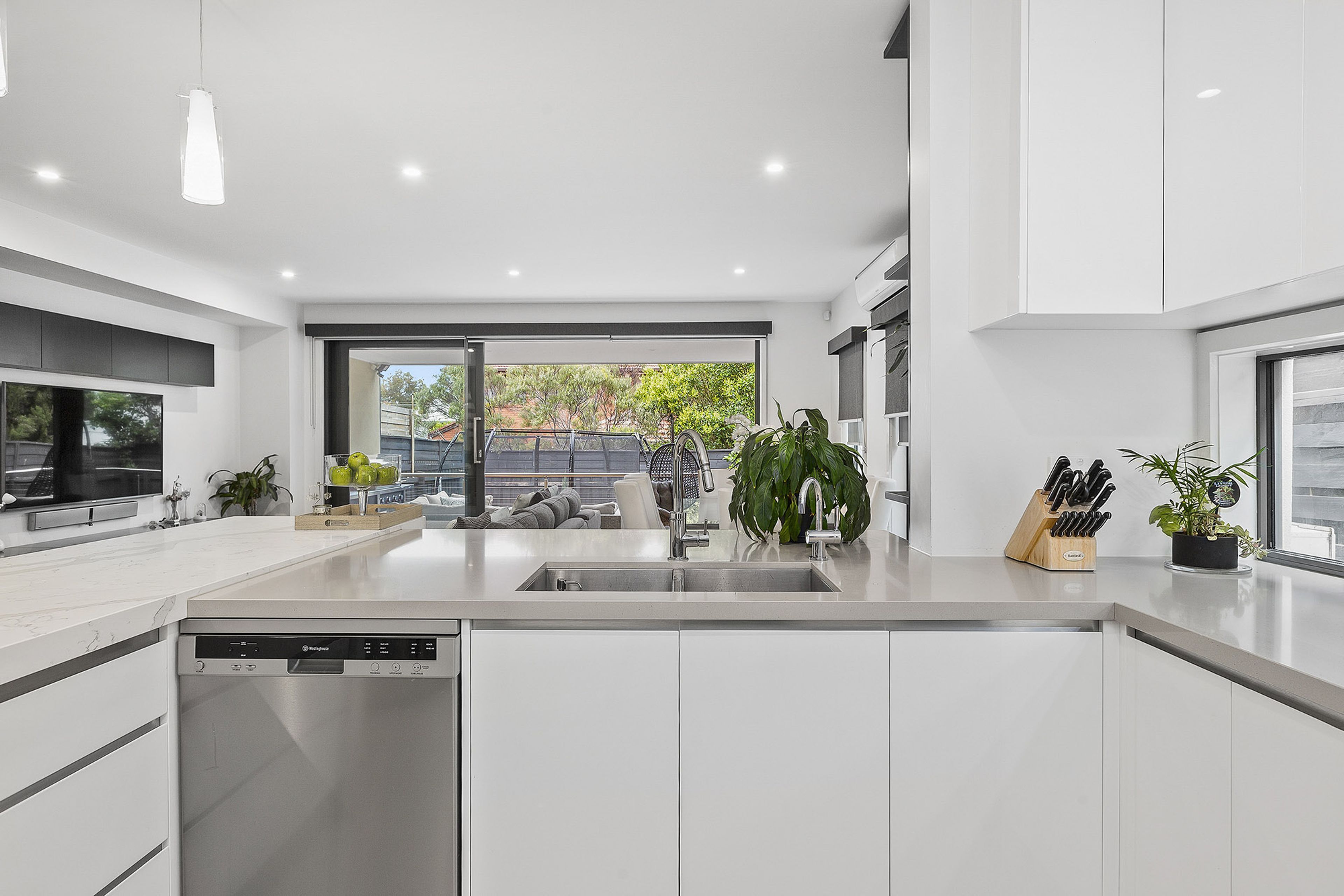 A modern kitchen with a dishwasher, a large window, and a view of the outdoors.