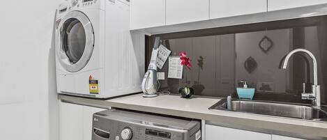 A compact kitchen with a washing machine, a dryer, a sink, and a small countertop.