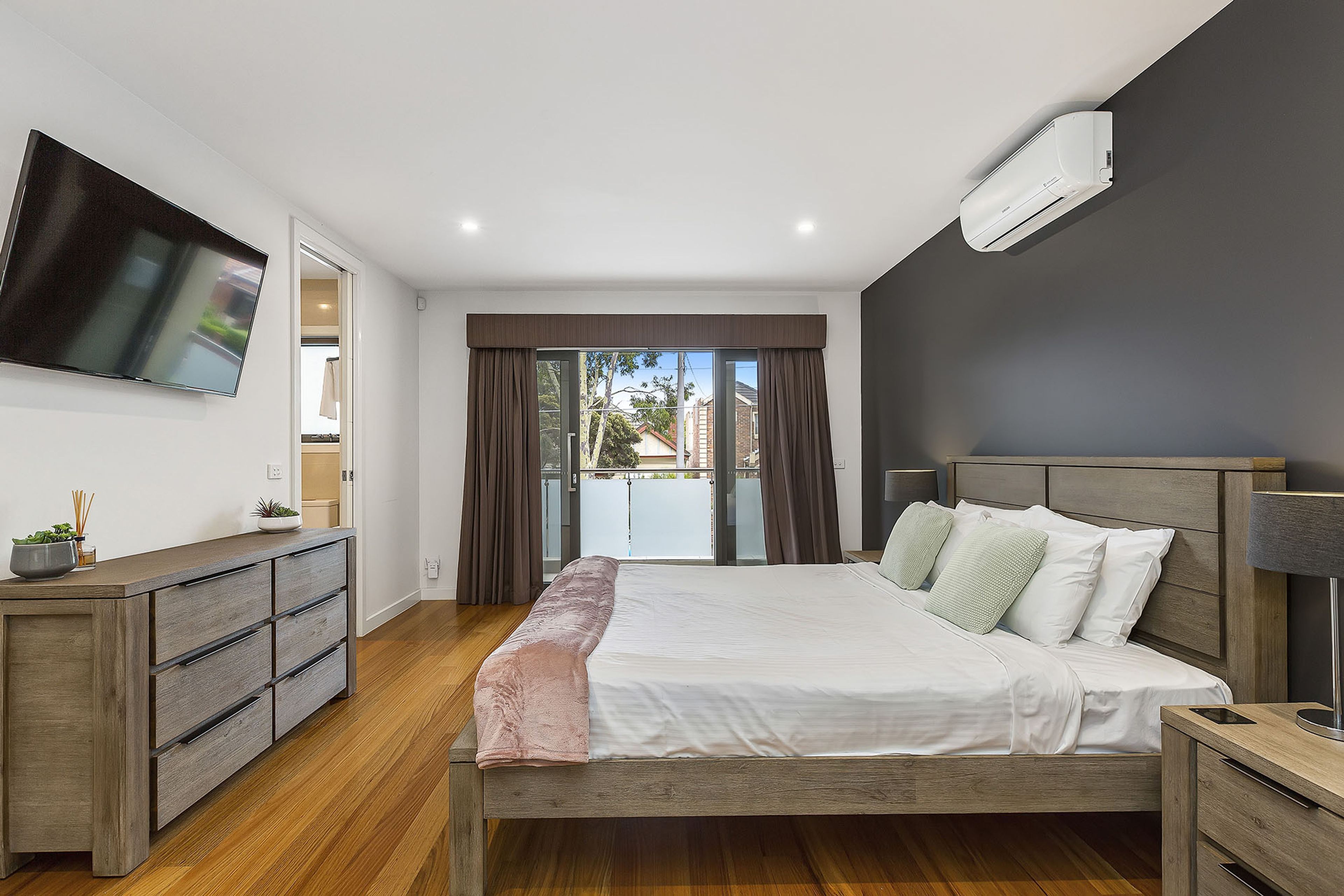 A modern bedroom with a bed, a TV mounted on the wall, a bedside table, and a window with curtains.
