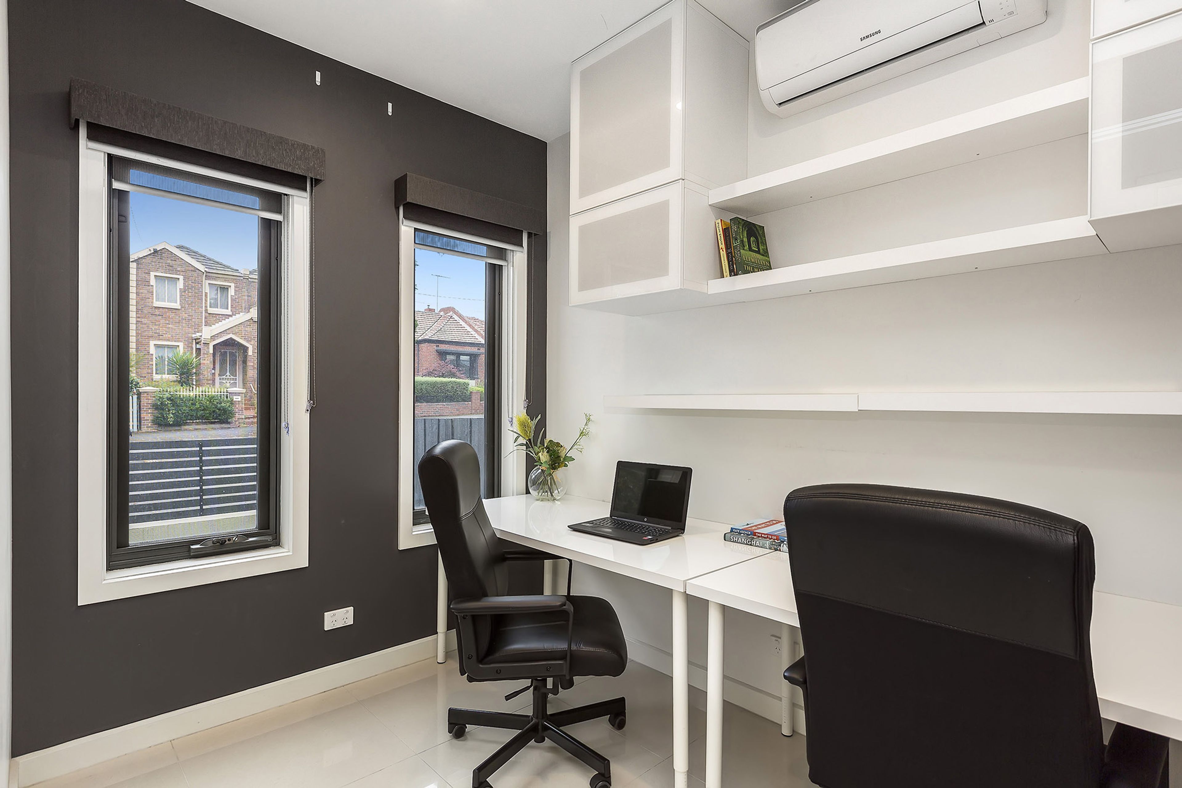 A modern office space with a desk, two black office chairs, a laptop, and a bookshelf.